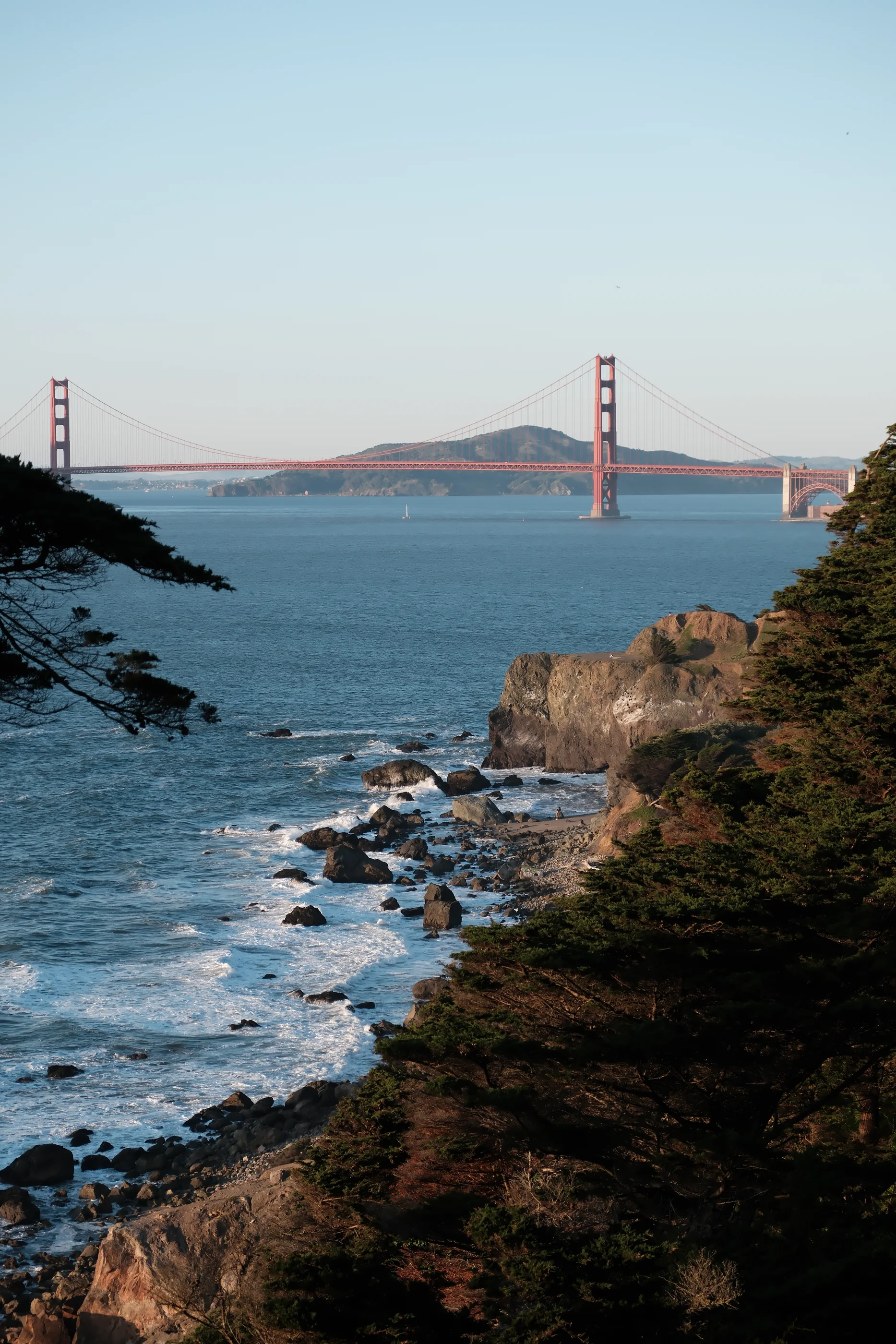 The Golden Gate Bridge beyond the rocky shoreline and cypress trees at Lands End
