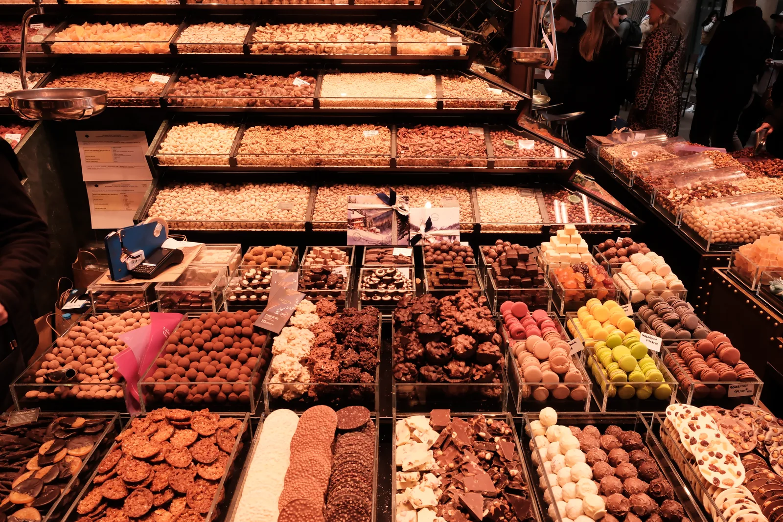 A market counter neatly arranged with chocolates, cookies, truffles, and colorful macarons
