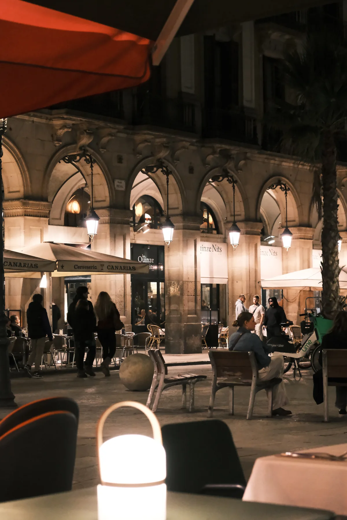 Restaurant tables and softly lit stone arcades around Plaça Reial at night
