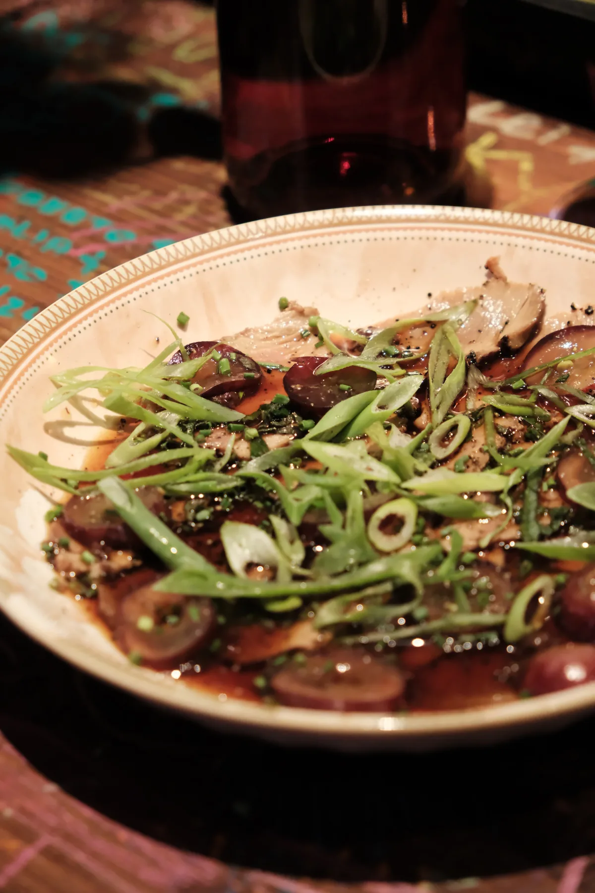 A glossy small plate of thinly sliced seared fish with grapes, scallions, and herbs