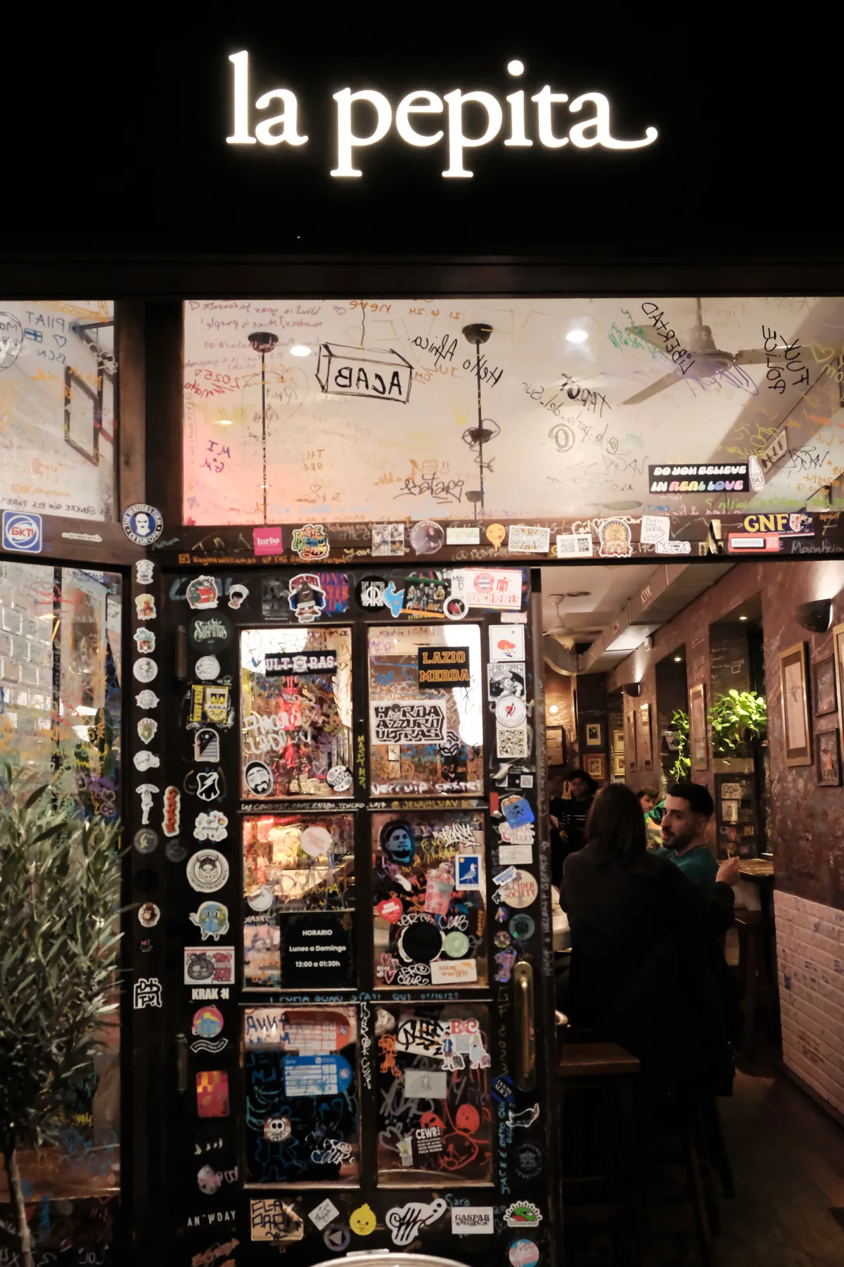 The sticker-covered entrance and illuminated La Pepita sign in Barcelona at night