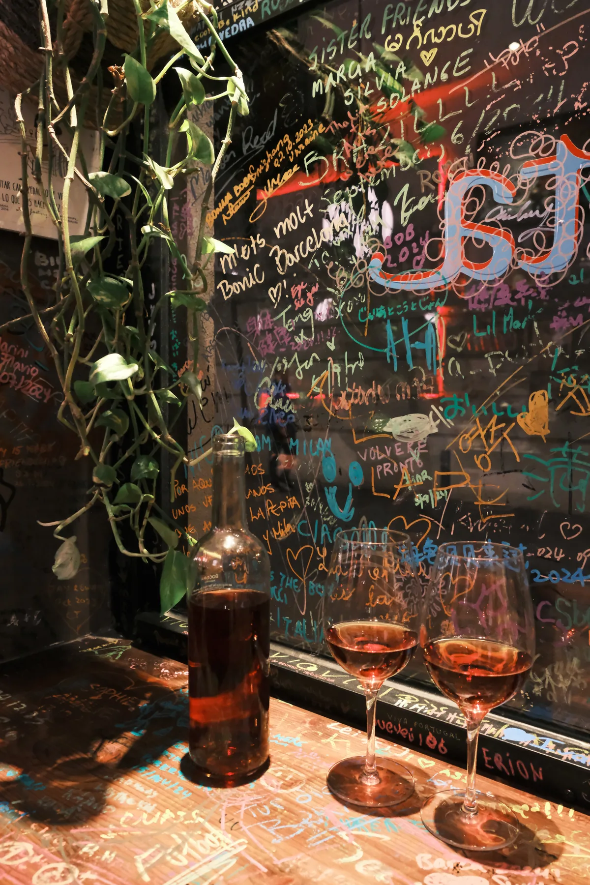 A bottle and two glasses of rosé beside La Pepita's colorful signature-covered wall