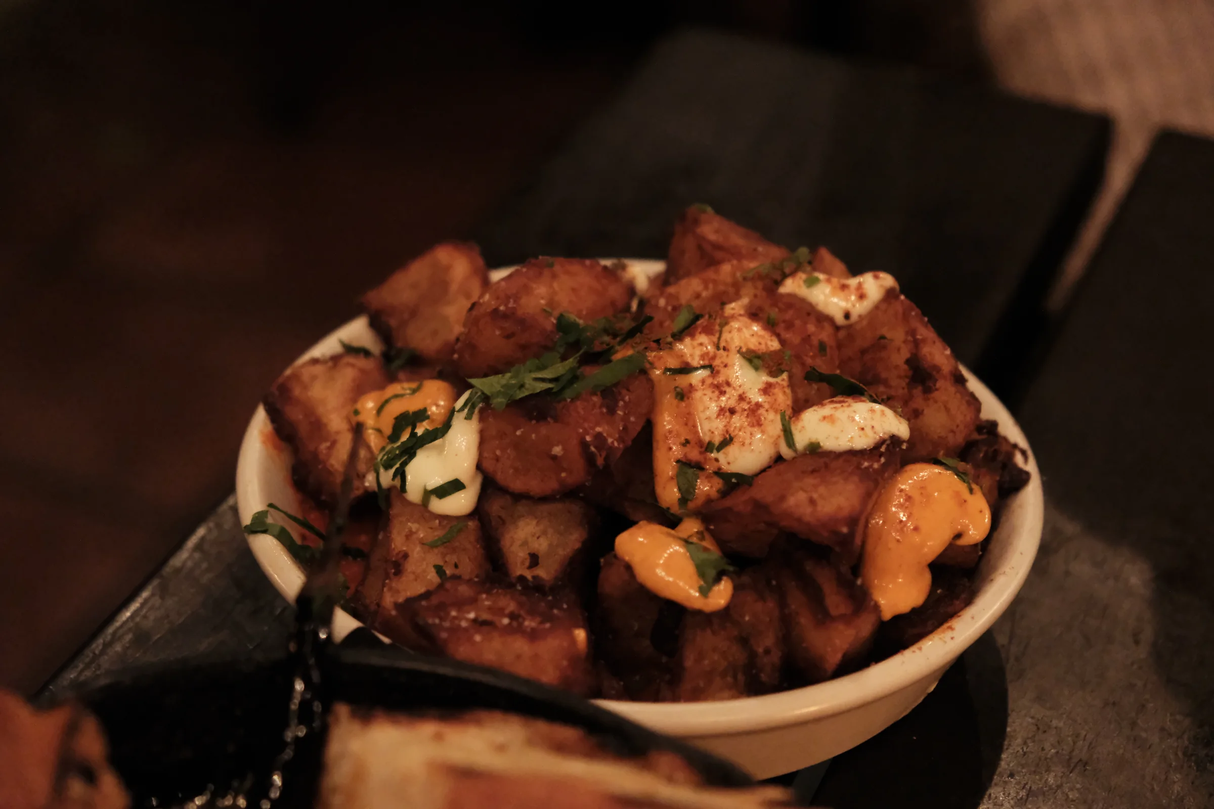 A bowl of patatas bravas finished with two sauces and herbs