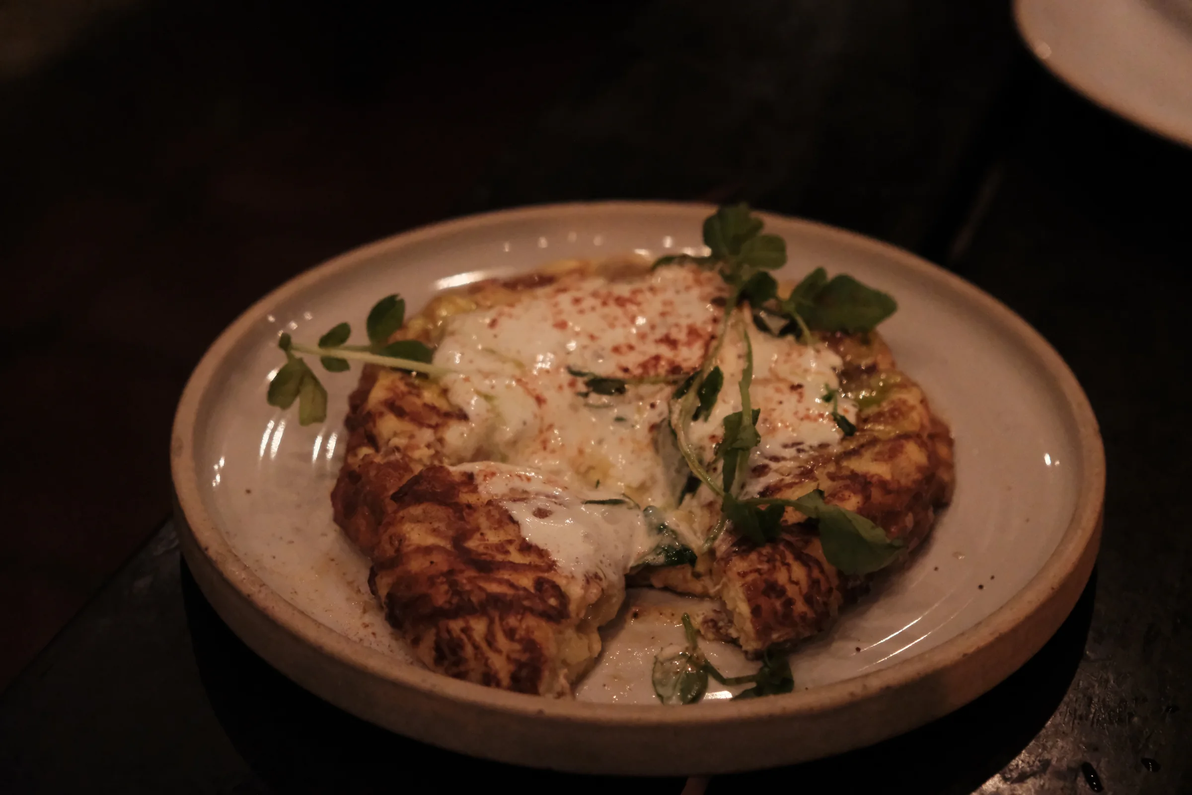 A Spanish tortilla topped with a creamy sauce and fresh herbs