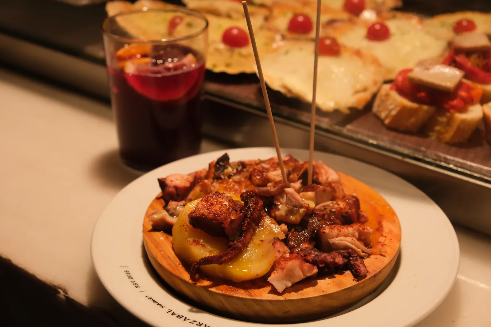 A plate of octopus and potatoes beside a glass of red sangria