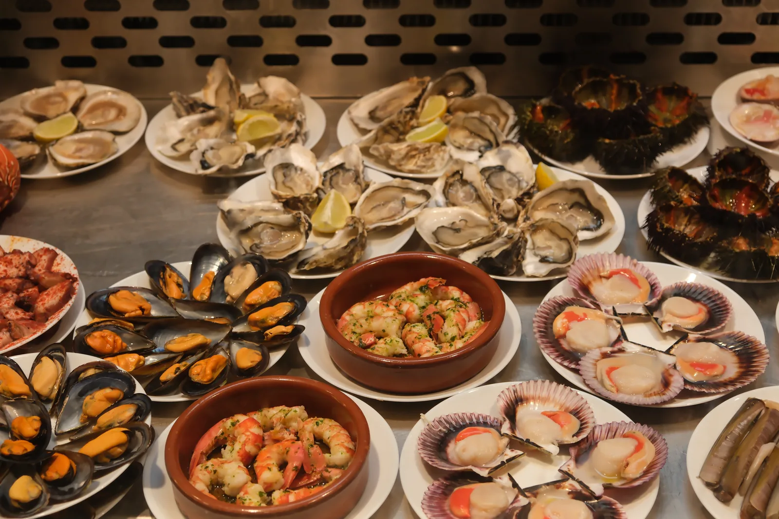 A seafood counter covered with oysters, mussels, scallops, prawns, octopus, and sea urchins