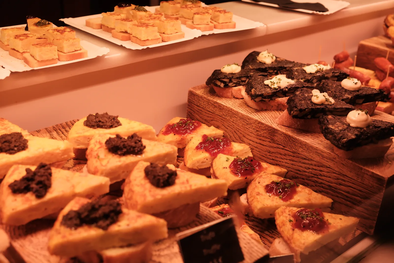 Several styles of Spanish tortilla arranged on wooden boards at a market counter
