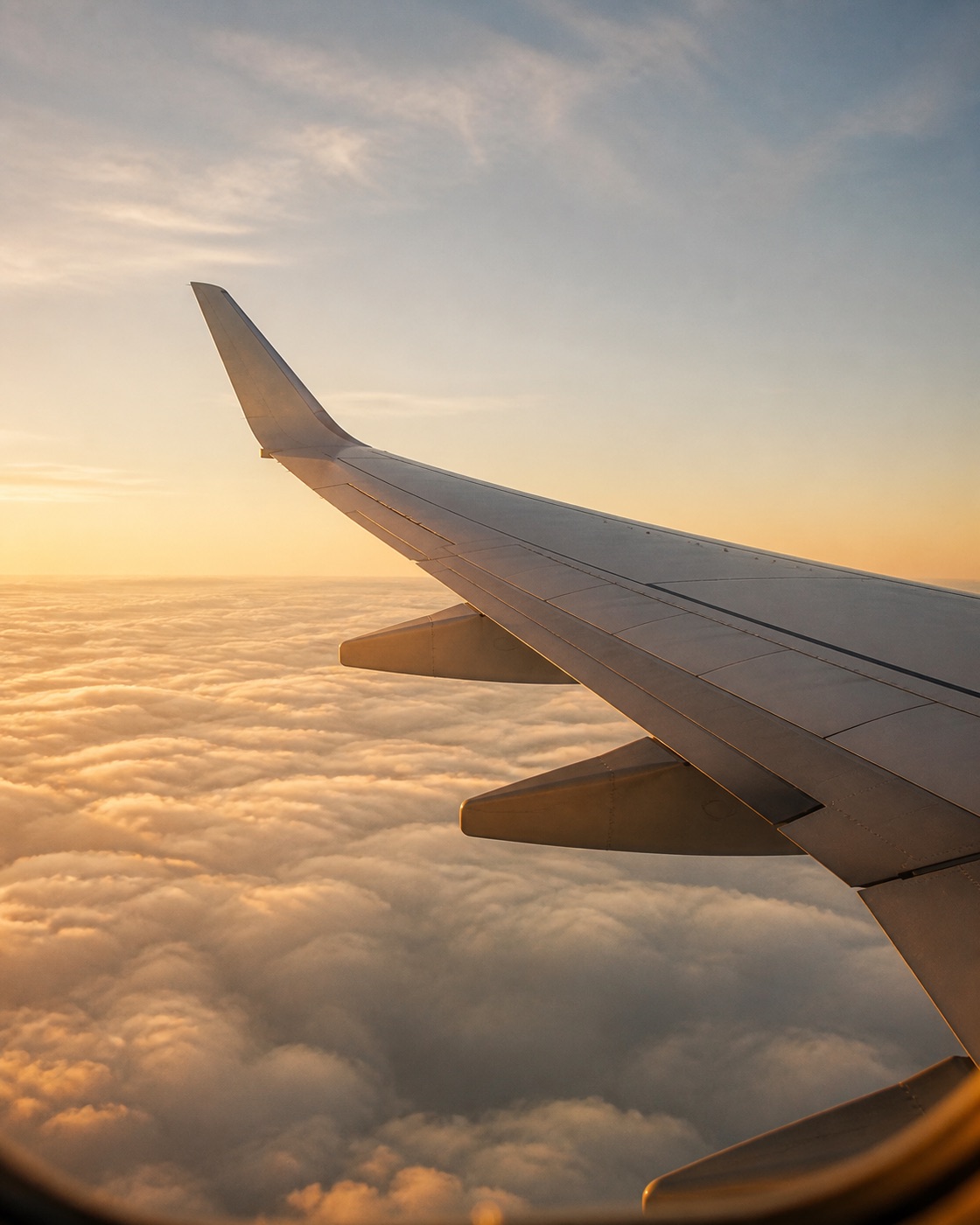An airplane wing above soft clouds in warm late-afternoon light