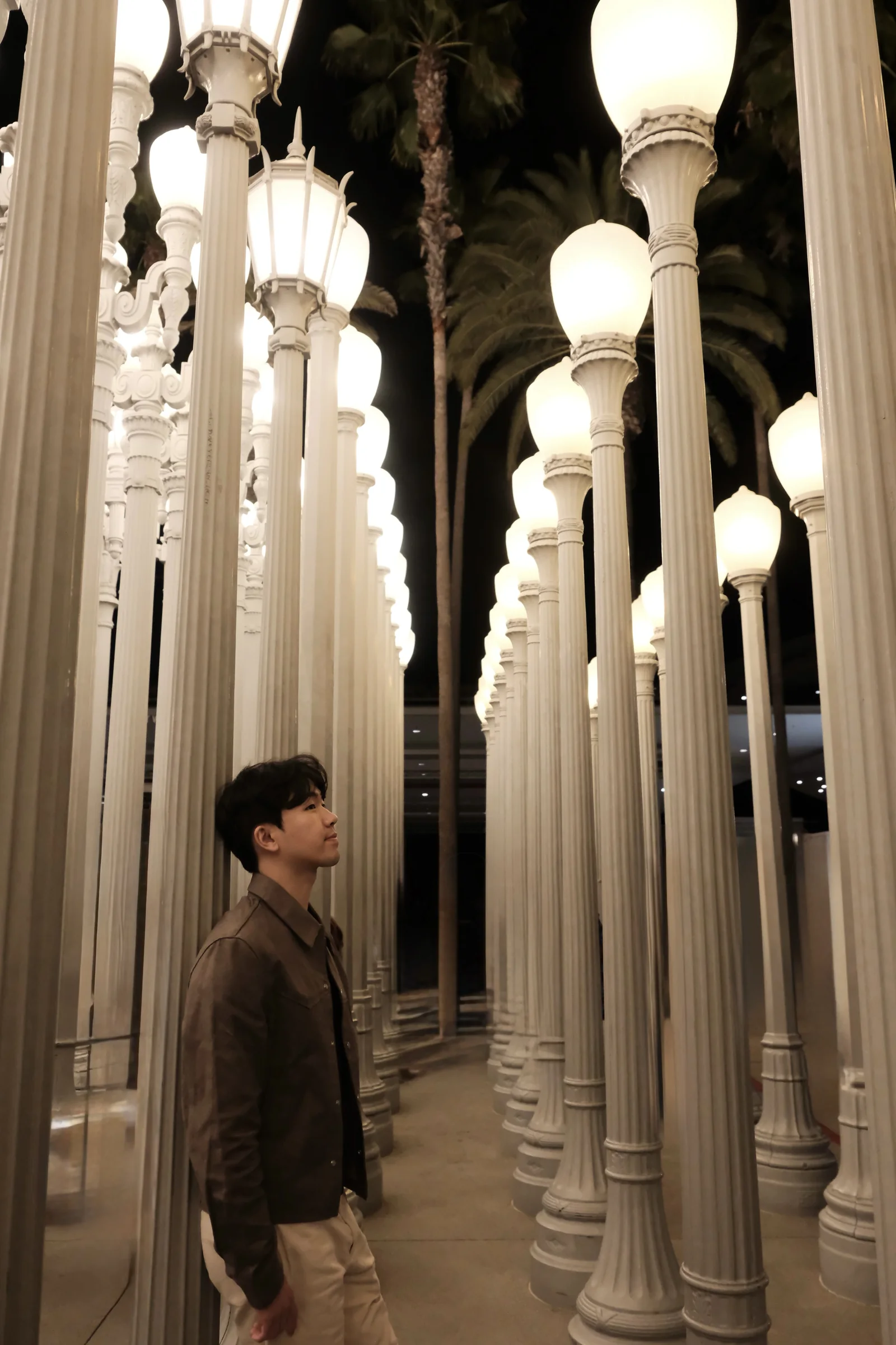 Shawn standing among rows of illuminated street lamps at Urban Light in Los Angeles