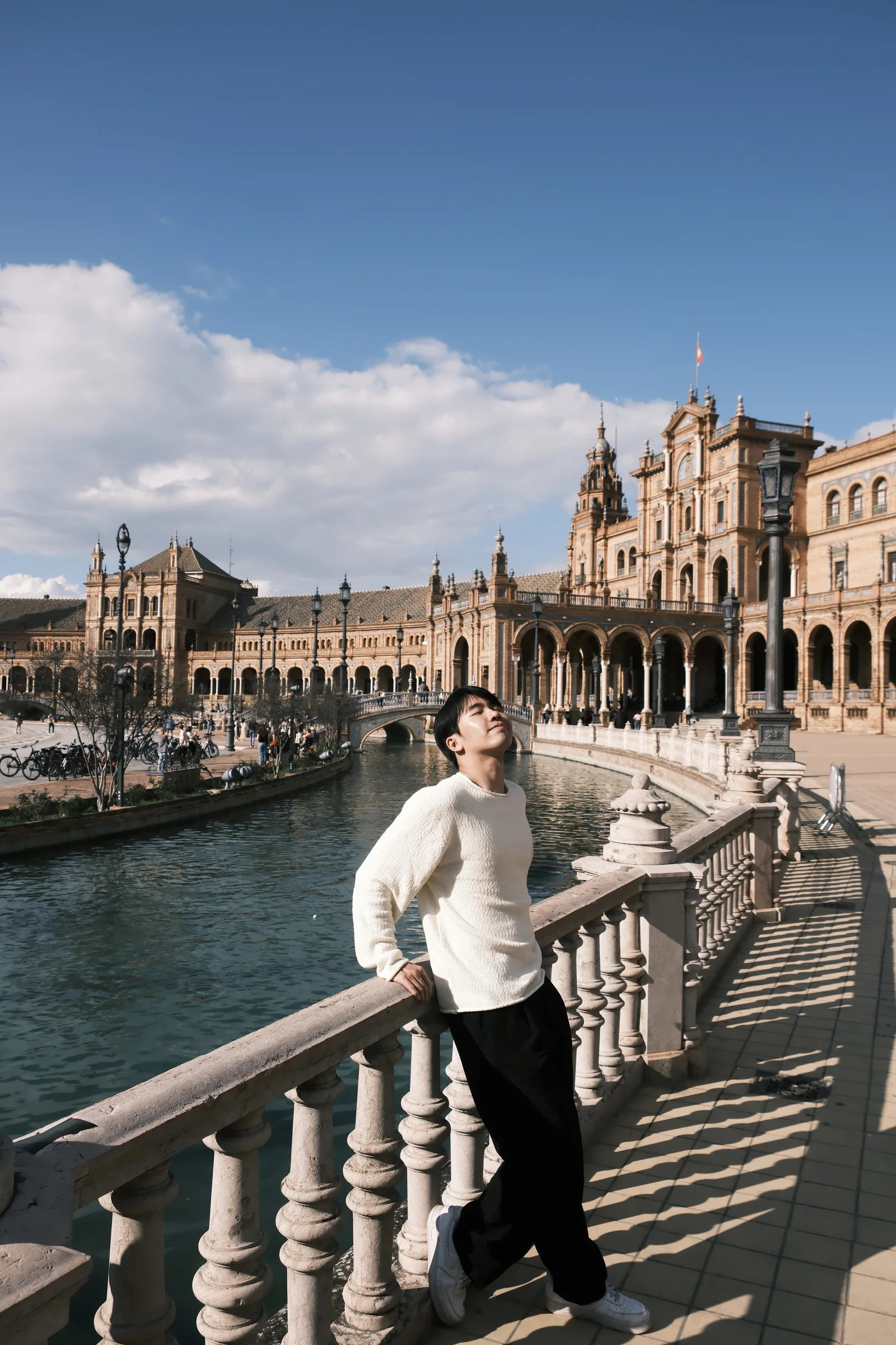 Shawn leaning against the tiled canal at Plaza de España under a bright blue sky