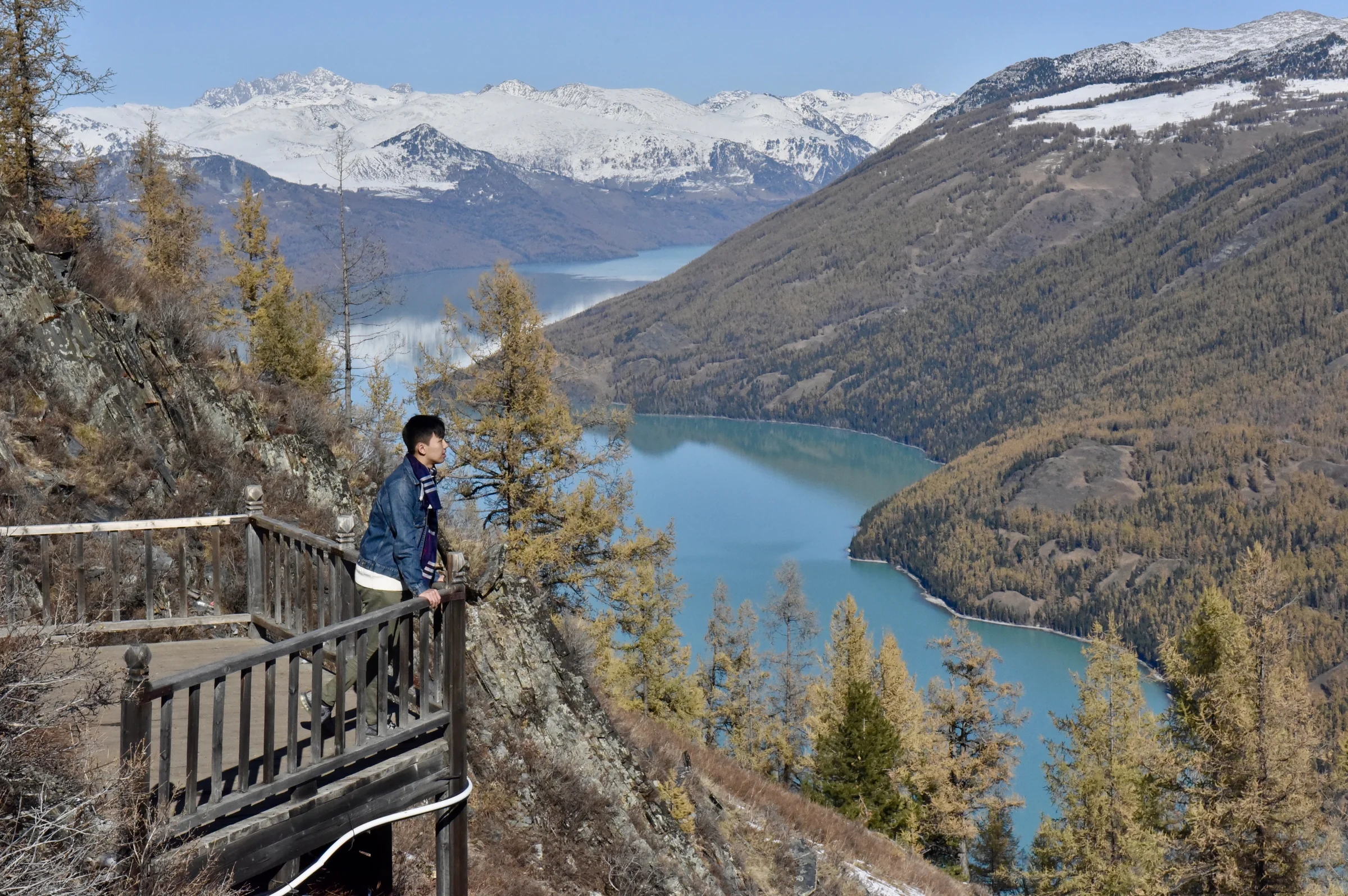 Shawn standing at an overlook above a blue lake edged with golden autumn trees