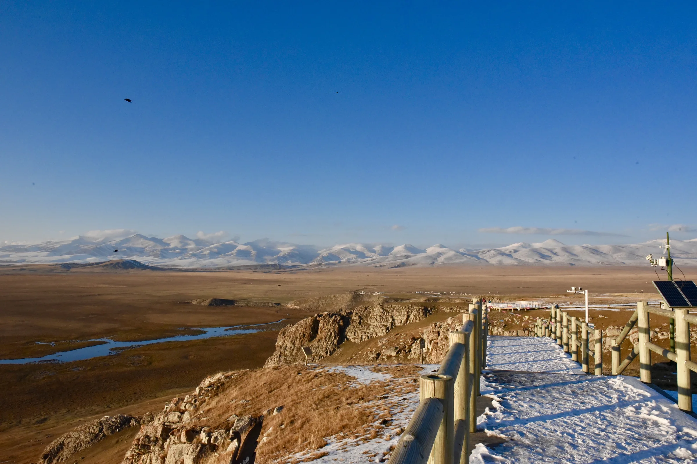 A high roadside overlook opening onto plains, lakes, and distant mountains