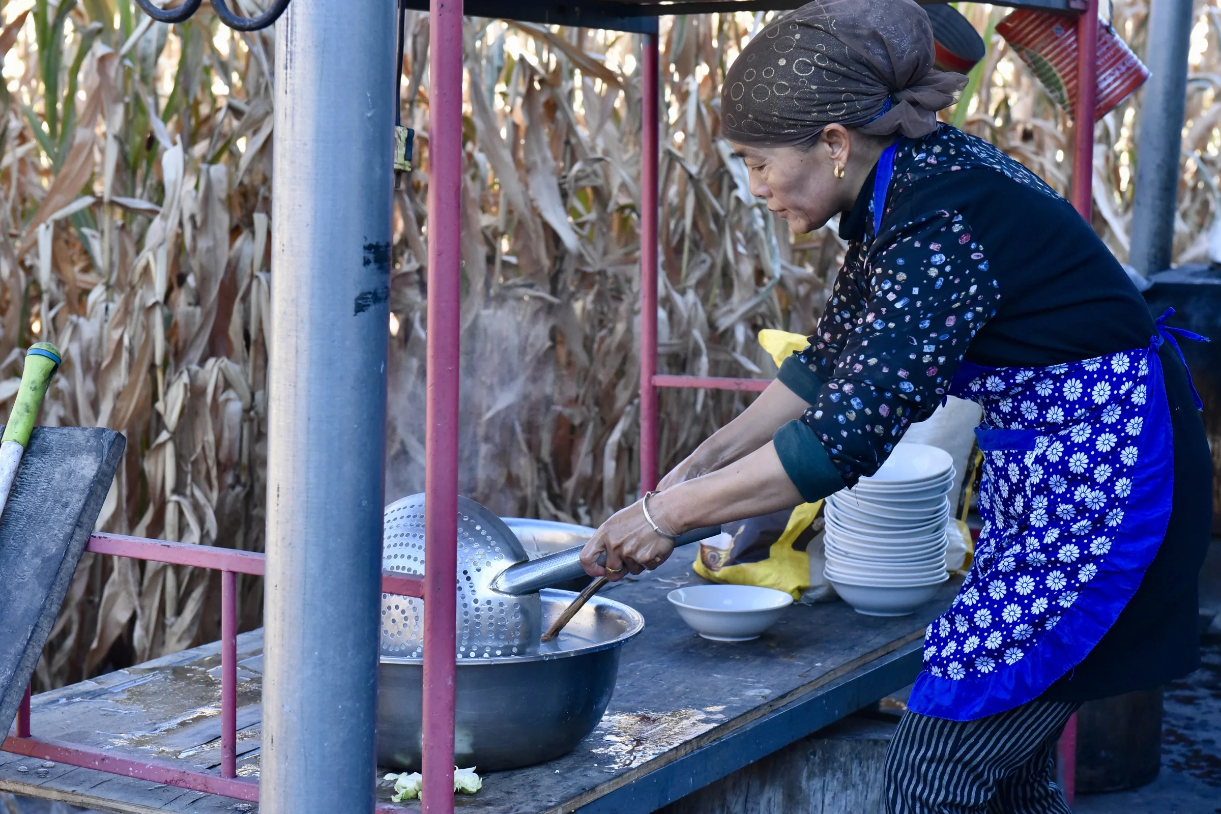 A woman preparing a meal outdoors beside a wooden shelter