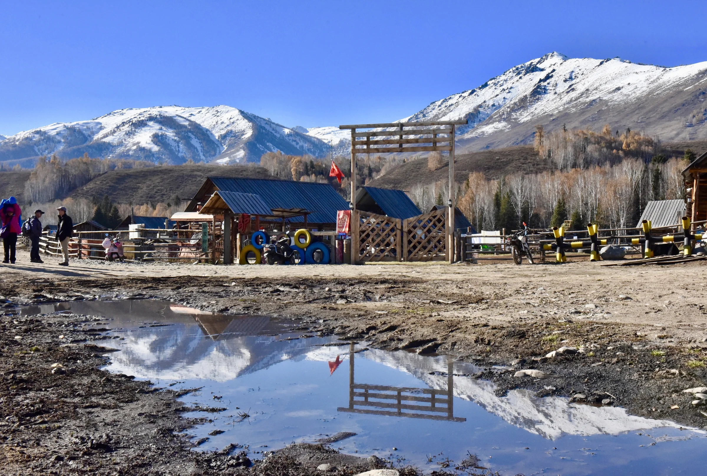 Snowy peaks reflected in a large puddle beside a mountain settlement