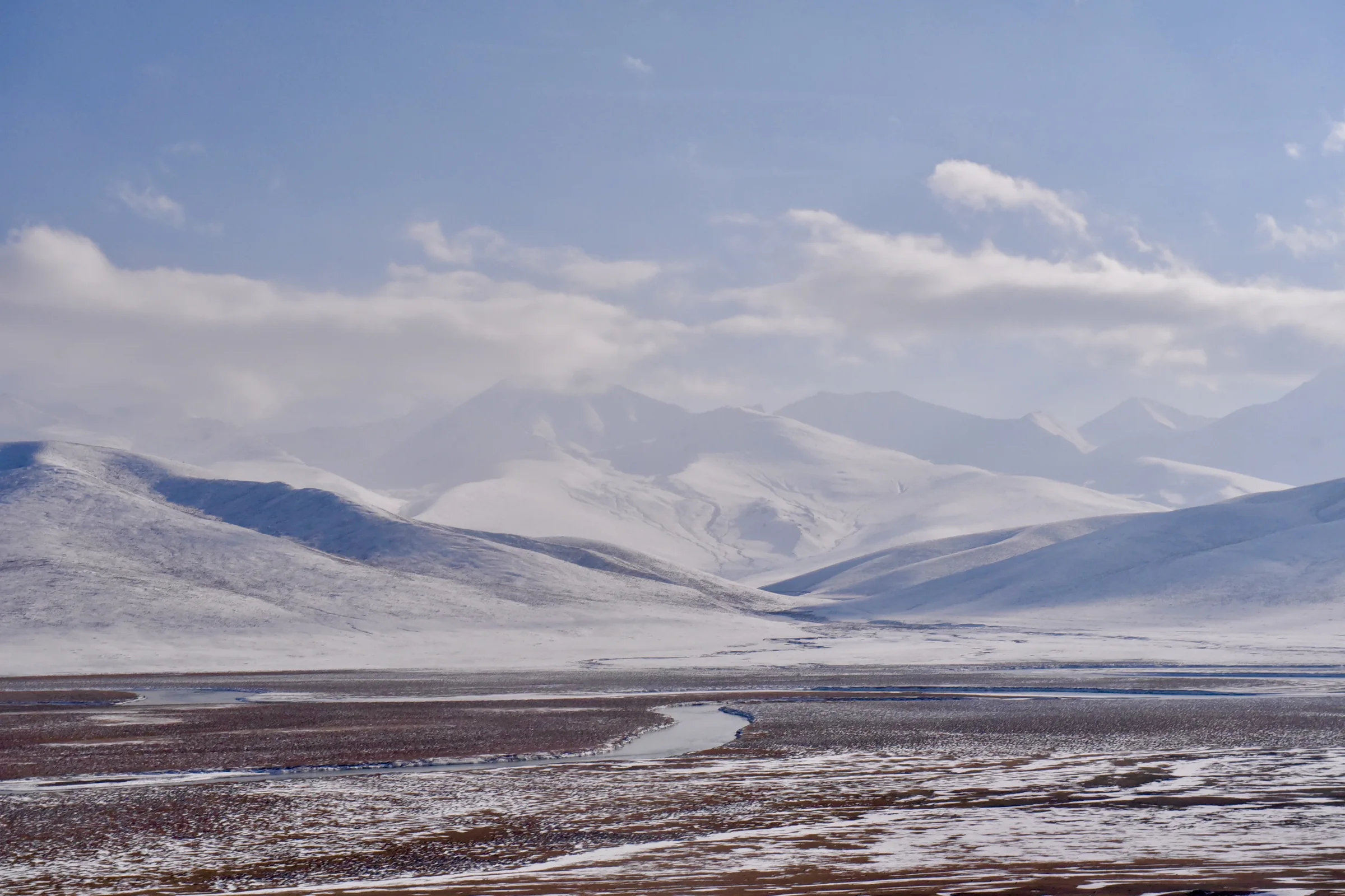 Layered snowy mountains fading into pale evening light