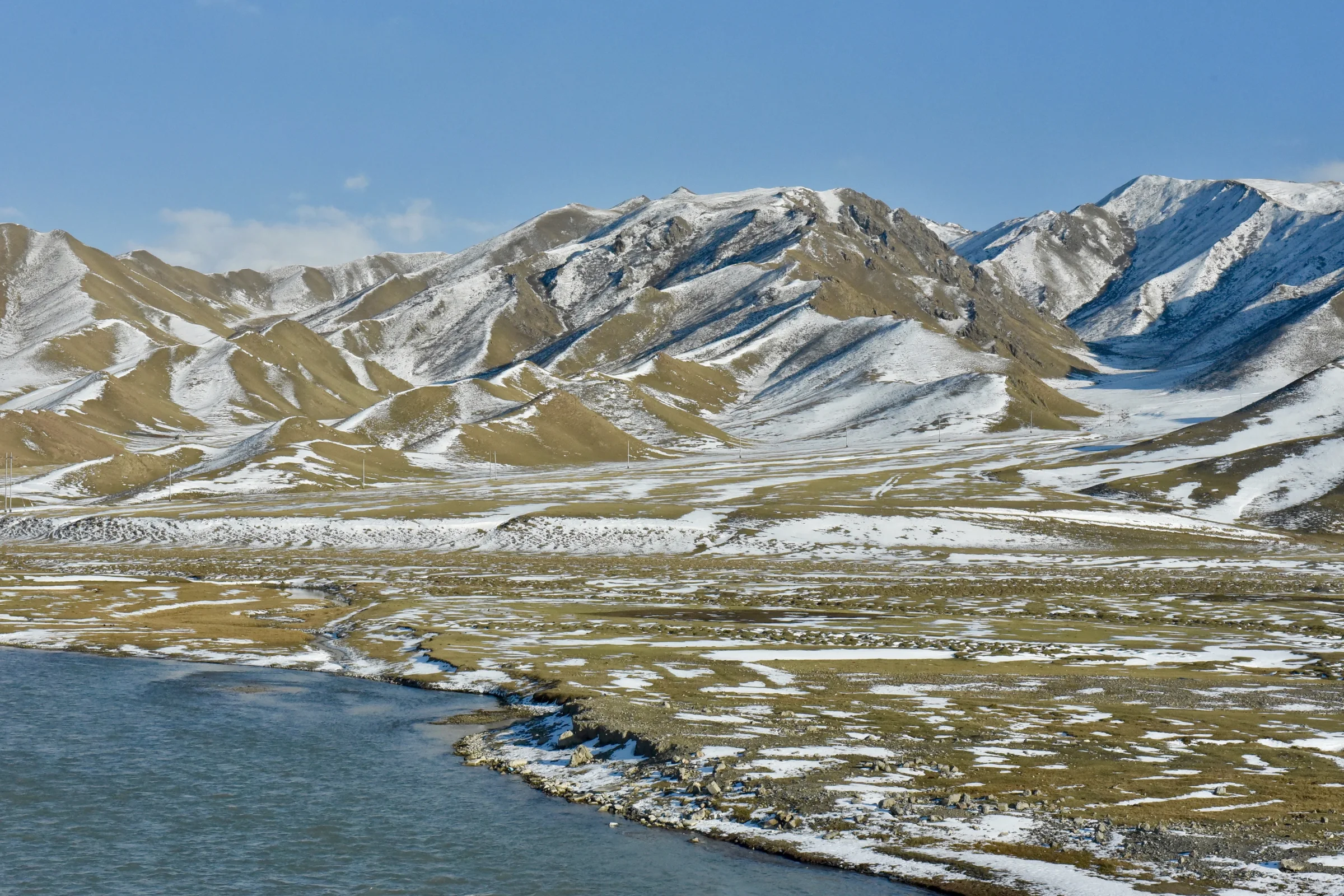 A blue river winding through foothills lightly covered in snow