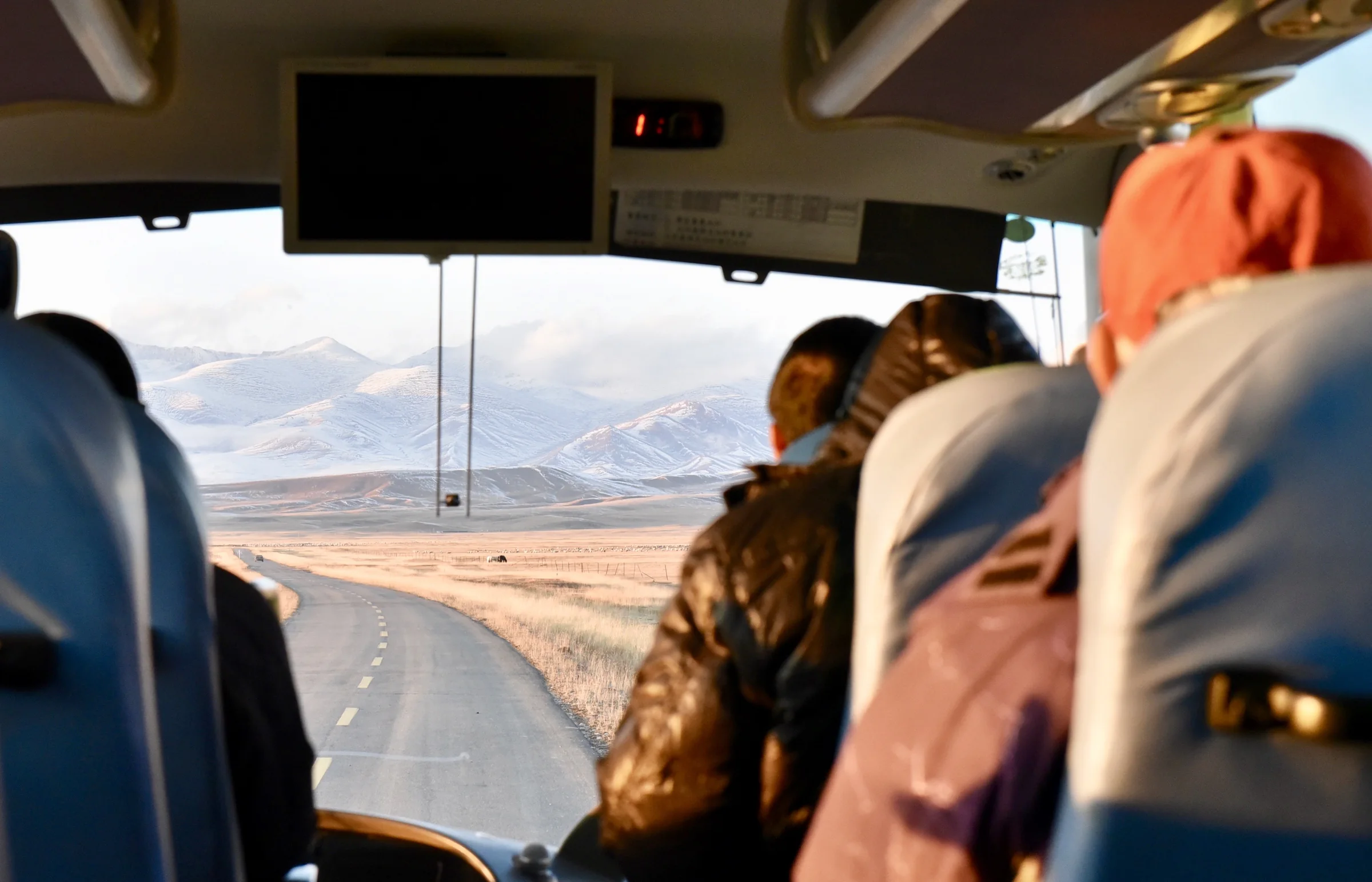 A winding mountain road seen through the warm interior of a bus